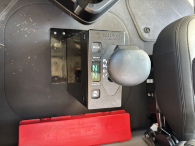 Cab interior showing Allison transmission shift module with gear indicator N N R, and mode/select buttons, mounted beside seat in Mack GR64B cab chassis.
