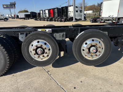 Dual rear axles on a Mack GR64B cab and chassis showing steel wheels and tires, framed undercarriage, and a row of trucks in the background.