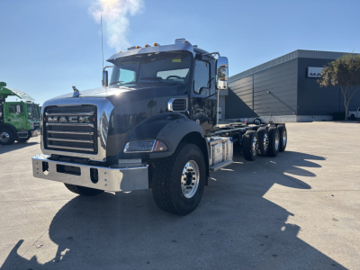Mack GR64B cab and chassis truck in a dealership lot, front three-quarter view with chrome bumper and grille, 6x4 configuration, large side mirrors.