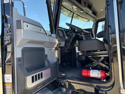 Cab and chassis interior of a 2025 Mack GR64B showing driver seat, steering wheel, dashboard, and a red fire extinguisher on the floor.