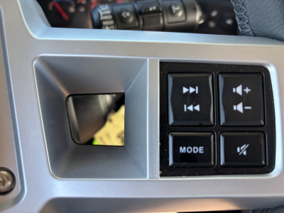 Dashboard control panel with square buttons including mode and speaker icons; partial view of steering wheel and instrument cluster.