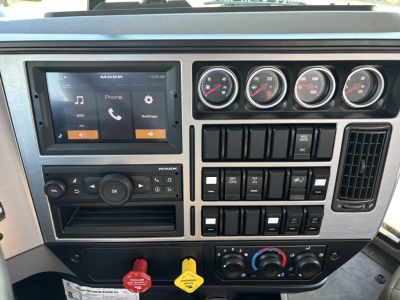 Dashboard view of a 2025 Mack GR64B cab and chassis interior showing a touchscreen infotainment system, multiple gauge cluster, climate controls, and various switches.