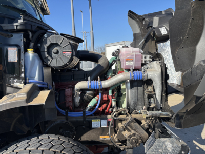 Engine bay of a new 2025 Mack GR64B cab and chassis showing coolant reservoir, hoses, and turbo/intercooler components.