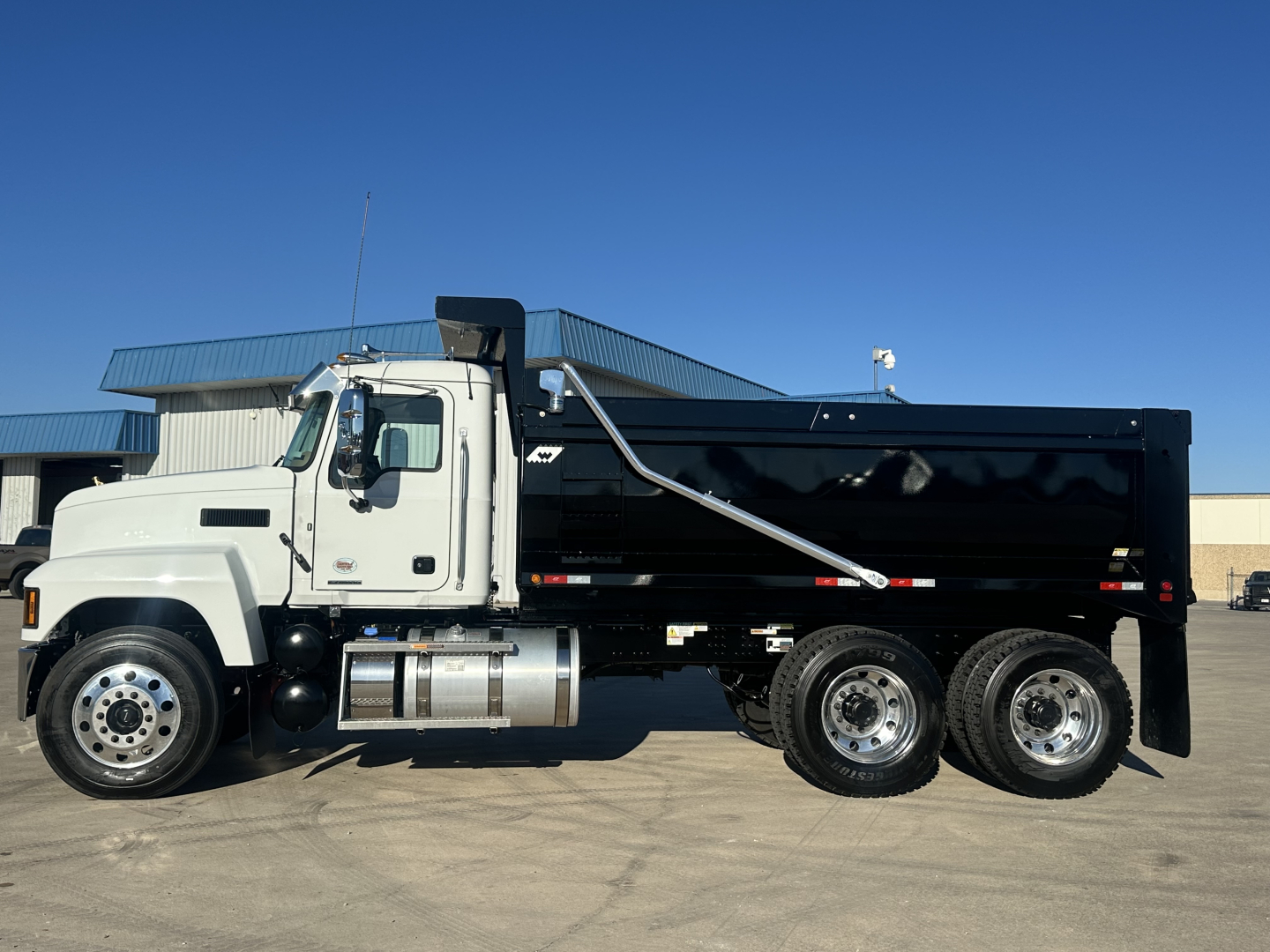 Mack PI64 dump truck in side profile view showing white cab and black dump body with three rear axles.