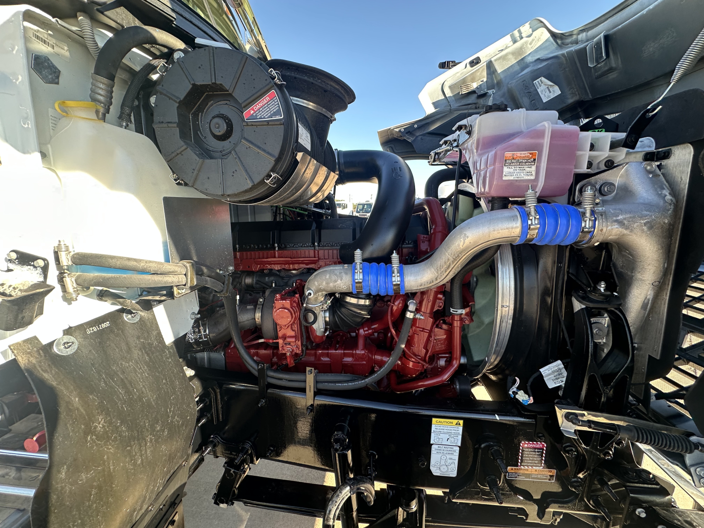 Mack PI64 engine bay showing turbocharger, hoses, coolant reservoir, and pink coolant overflow bottle.