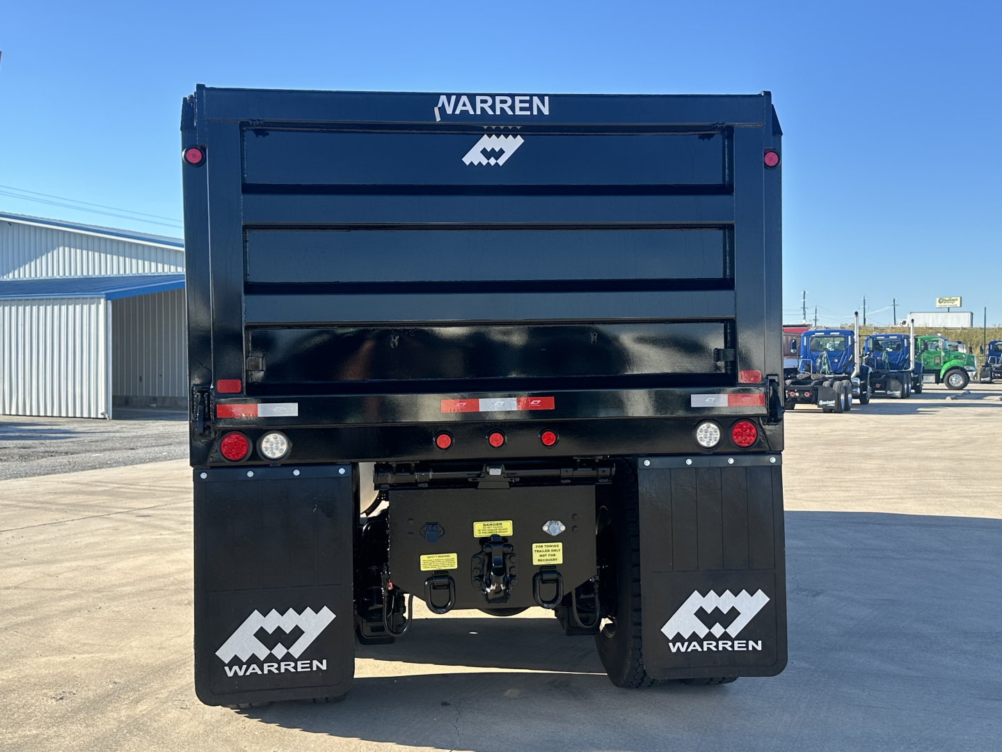 Rear view of a new Mack PI64 dump truck with Warren branding on mud flaps and rear bumper. Tailgate area with lights and hitch components visible.