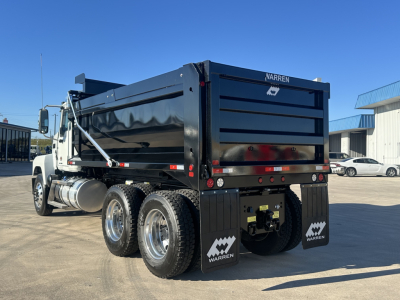 Mack PI64 dump truck viewed from rear-left, black dump body with Warren branding, dual rear axles, chrome fuel tank, spare wheels, and mud flaps.