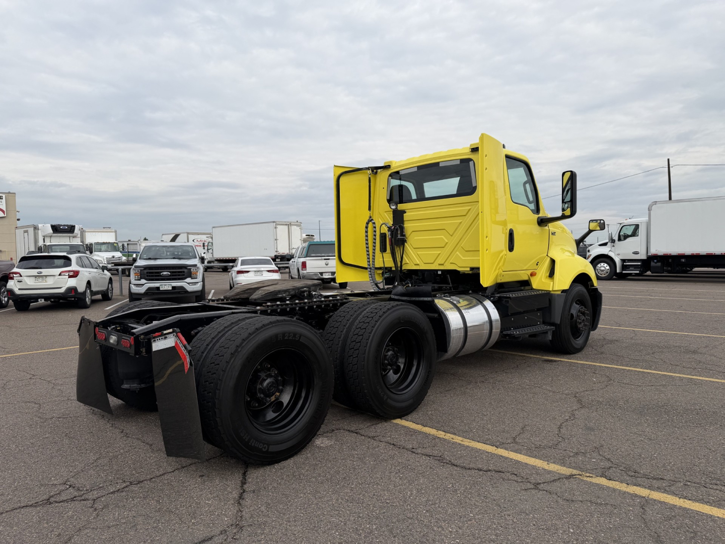 Yellow 2023 International LT625 daycab tractor chassis with dual rear axles and fuel tank, outdoor lot background