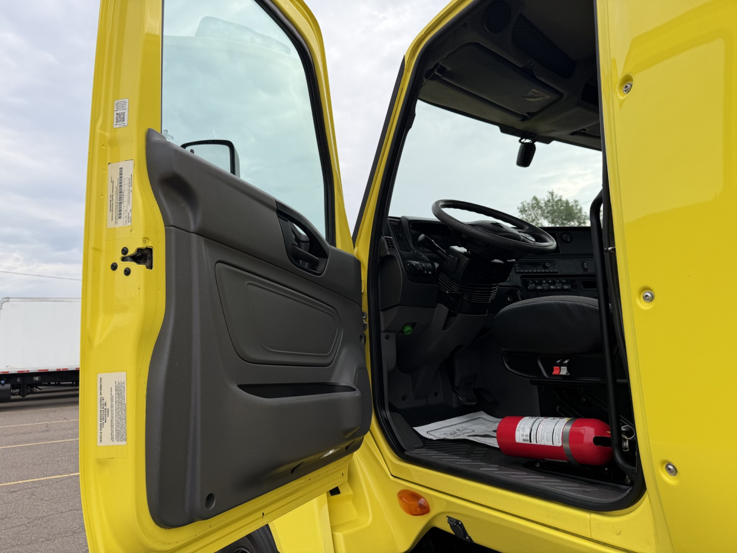 Cab entry of a yellow 2023 International LT625 Daycab showing open driver door with interior dashboard and steering wheel visible.
