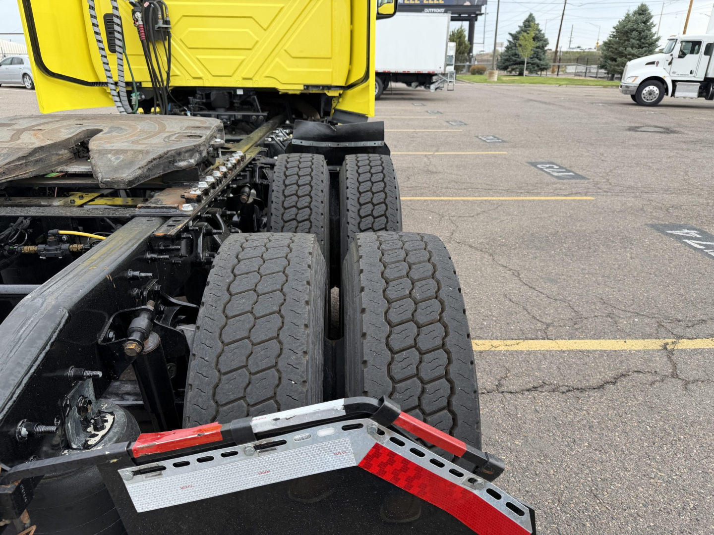 Tractor-trailer rear wheels and chassis showing dual rear axles and fifth wheel mounting on a yellow cab.