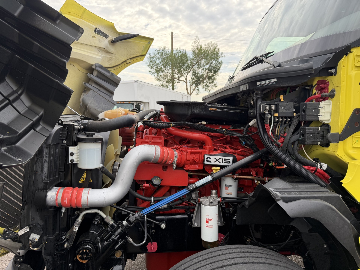 International LT625 engine bay showing red engine with X15 badge, white filters, hoses, and yellow truck body in view.