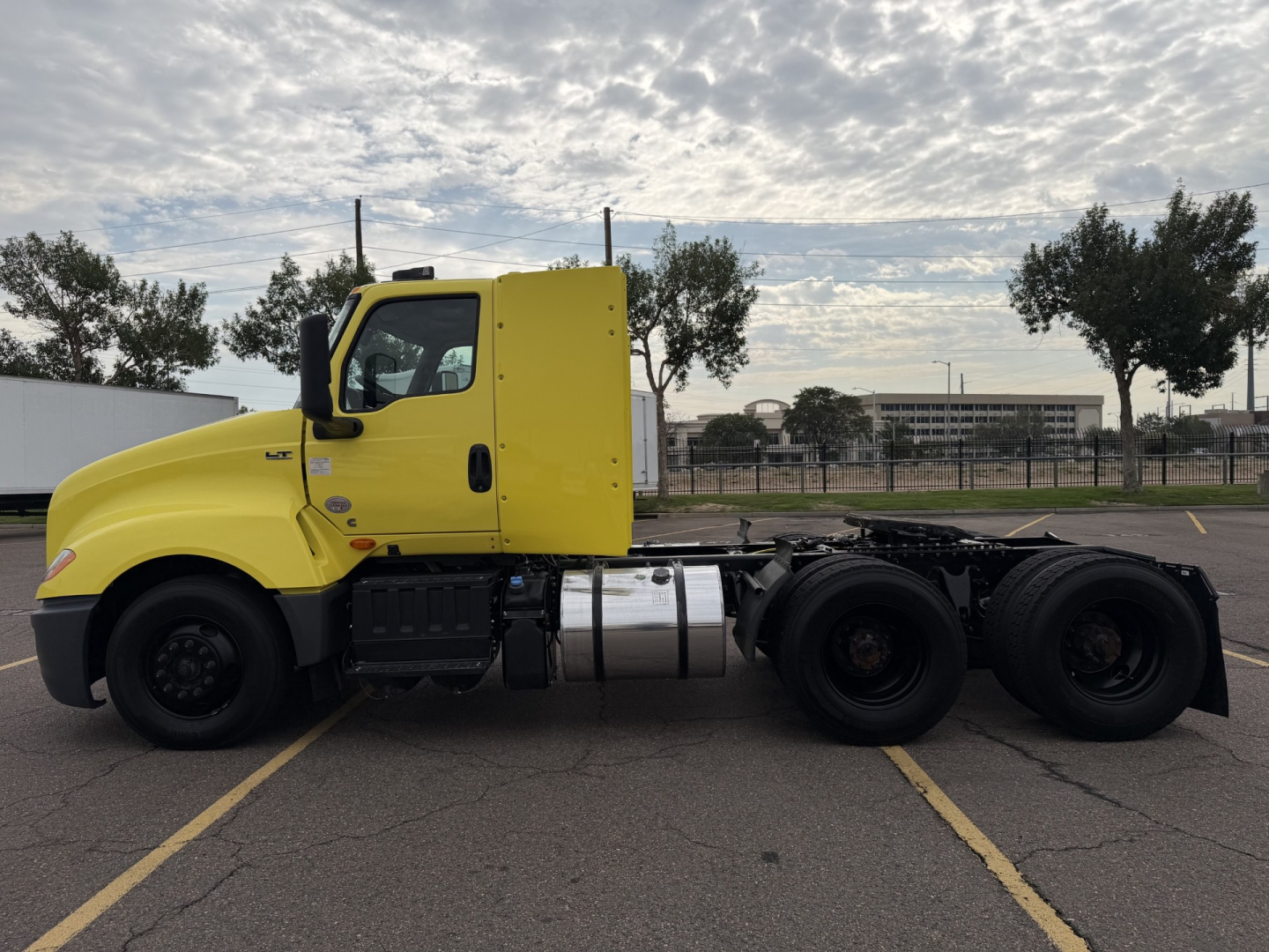 Truck side view of a yellow 2023 International LT625 cab over semi-truck in a parking lot, showing chassis and rear axle configuration.