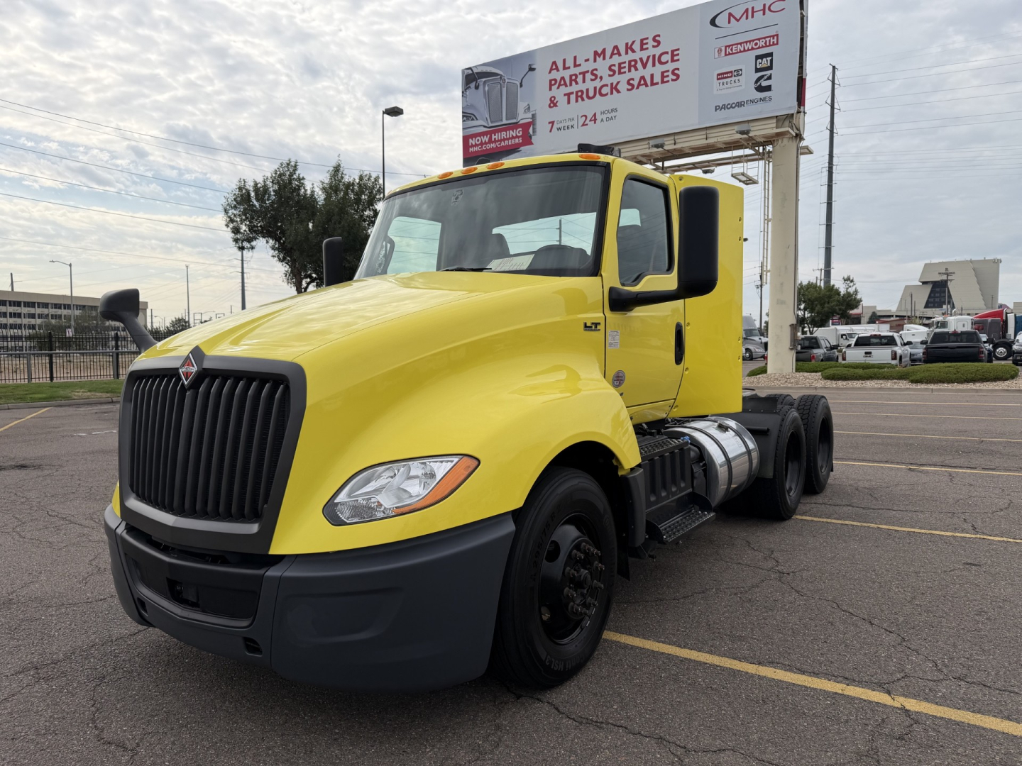 Truck with yellow cab 2023 International LT625 conventional daycab in a parking lot, front-left view, showing large black grille and dual rear axle setup.