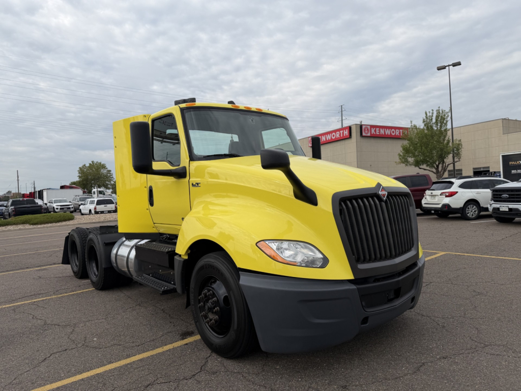 Yellow 2023 International LT625 conventional daycab truck with black front grille, large mirrors, and dual rear axles in a dealership lot.