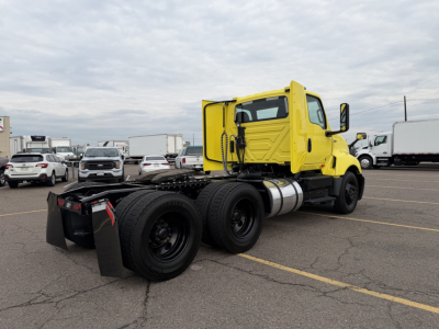 Yellow 2023 International LT625 daycab tractor chassis with dual rear axles and fuel tank, outdoor lot background
