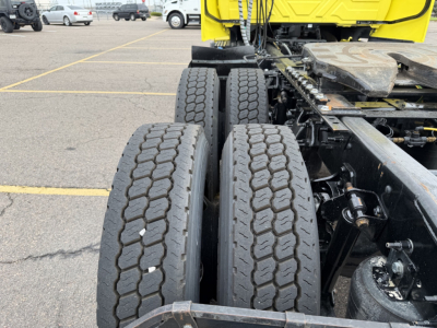 Rear view of a truck chassis showing dual rear tires and part of the cab in yellow; visible components include the suspension, drive axle, and frame.