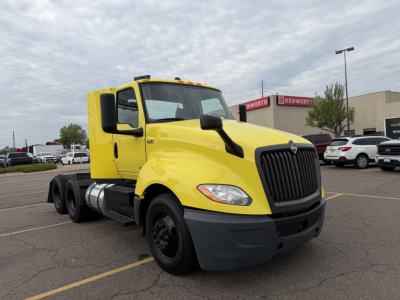 Yellow 2023 International LT625 conventional daycab truck with black front grille, large mirrors, and dual rear axles in a dealership lot.