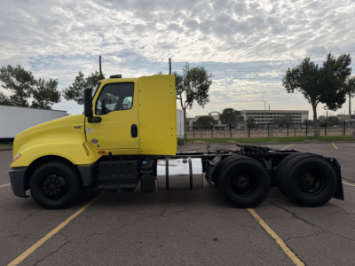 Truck side view of a yellow 2023 International LT625 cab over semi-truck in a parking lot, showing chassis and rear axle configuration.