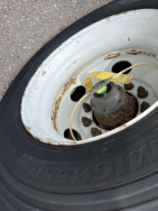 Trailer wheel with white rim, black tire, and yellow valve stem cap; rust spots on wheel hub area visible.