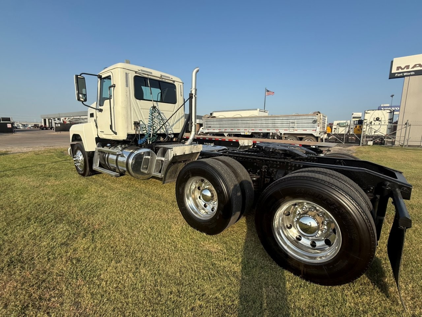 Mack PI64T truck chassis with dual rear axles showing front cab and bare frame, metal wheels, and exhaust stack in daylight.