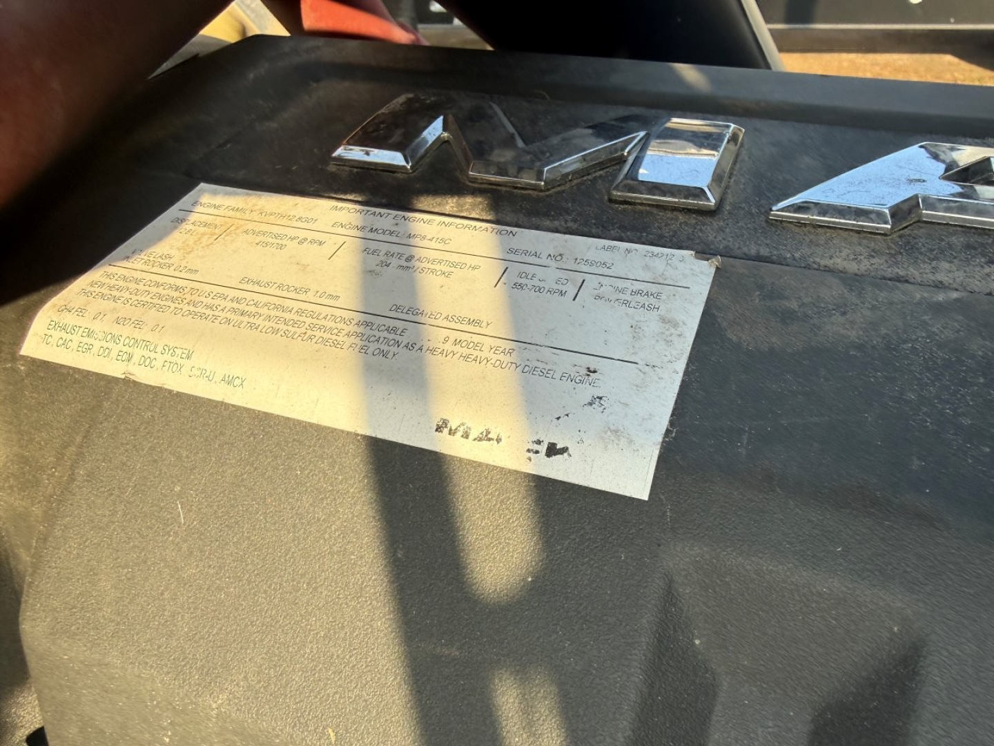 Truck dashboard with inspection label on the windshield showing Mack logo and data plate text visible.