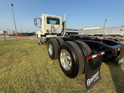 Truck chassis view of a 2020 Mack PI64T conventional daycab showing dual rear axles and fuel/air lines, with tires and Mack components visible.