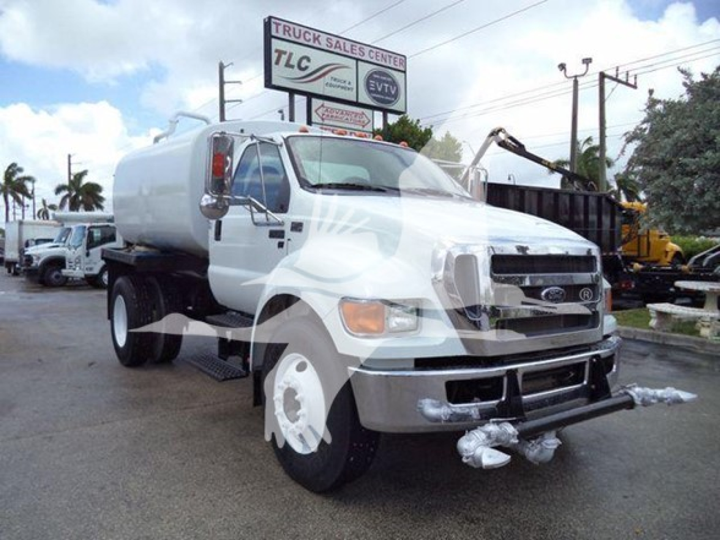 Front-left view of a white 2015 Ford F650 SD gas or diesel truck with a tanker body, showing front bumper, dual headlights, and side step; background includes dealership signage.