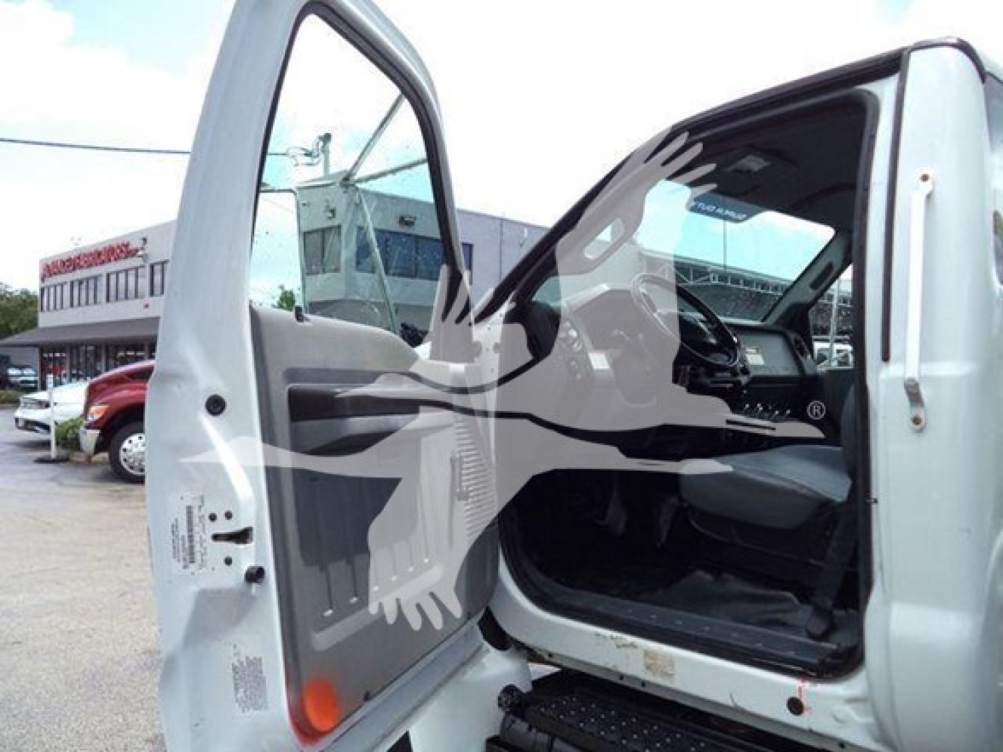 Ford F650 cab interior showing open driver door with steps, steering wheel, and dashboard visible. VIN sticker likely on door frame; background shows dealership lot.