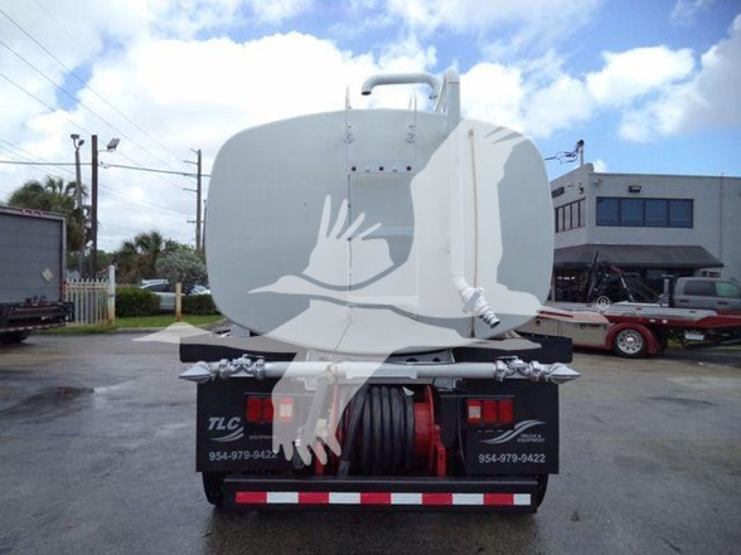 Truck fuel tank trailer back view with tank hoses and rear bumper; visible text on rear bumper area shows TLC and contact numbers; large white circular tank with ladder.