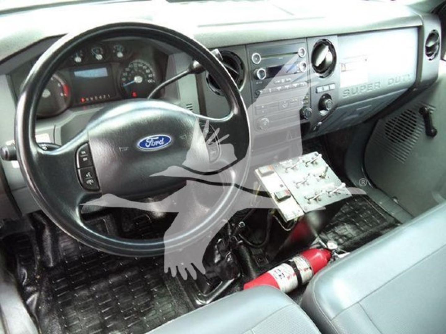 Ford dashboard interior showing steering wheel with Ford logo, instrument cluster, center console, and exposed wiring/remote panel near passenger side.