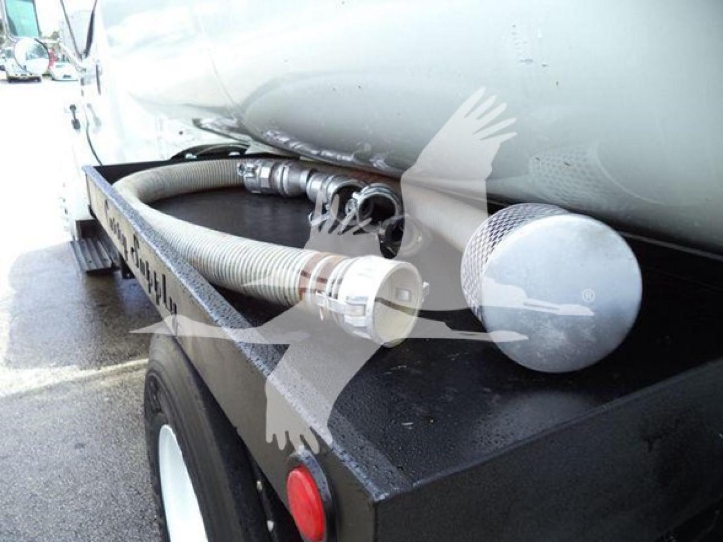 Truck fuel tanker with hoses and fittings mounted on side; visible hoses, metal fittings, circular cap; tank and wheel well in background.