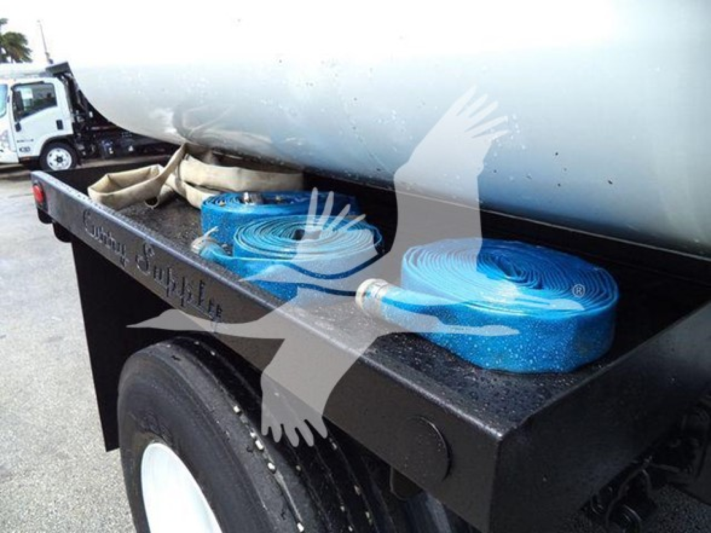 Truck bed with blue industrial hoses coiled and strapped, mounted under a cylindrical tank on a flatbed trailer.