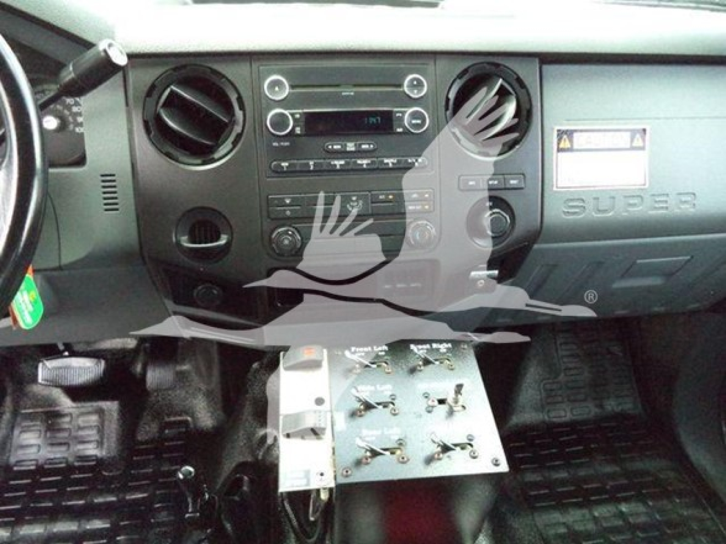 Dashboard view of a Ford Super Duty truck interior with climate controls and radio; metal control panel with switches mounted under the dash.