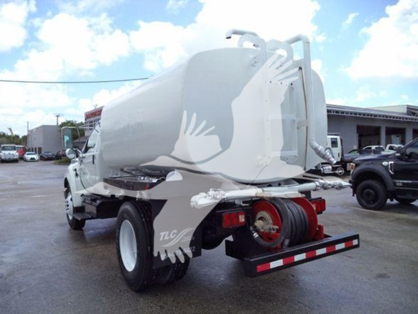 Truck-mounted water tanker with cylindrical tank, rear dual wheels, rear hose reel, and mirrored back view showing red chassis and bumper.