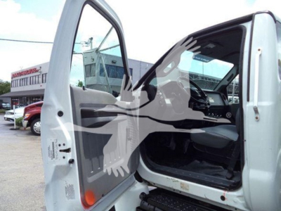 Ford F650 cab interior showing open driver door with steps, steering wheel, and dashboard visible. VIN sticker likely on door frame; background shows dealership lot.