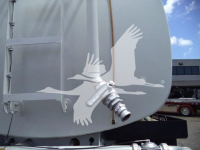 Truck cab or fuel tank with a large decorative bird graphic on the side and a chrome fitting protruding; background shows a building and another truck.