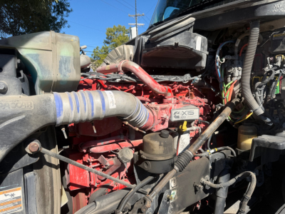 Kenworth T680 engine bay with red engine block, hoses, wiring harness, and air intake; visible components include X15 badge and coolant reservoir.