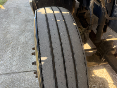 Kenworth T680 wheel/tire close-up showing tread and lug nuts, part of front wheel well in vehicle chassis.