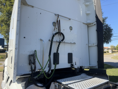 Kenworth T680 rear cab area showing fuel/air lines and electrical cables connected to back of trailer; entry steps and black protective wiring harness visible.