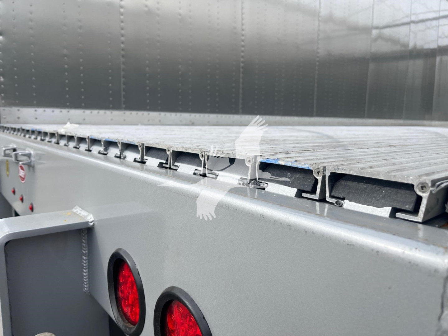 Trailer side view showing a metal walking floor deck with hinge slots and rear lighting on a Dorsey walking floor trailer.
