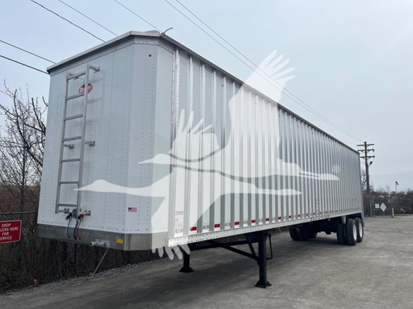 Trailer side view showing Dorsey walking floor trailer with silver corrugated sides and rear access ladder, dual rear axles, front landing gear visible.