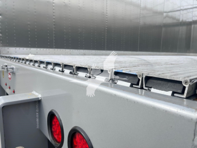Trailer side view showing a metal walking floor deck with hinge slots and rear lighting on a Dorsey walking floor trailer.