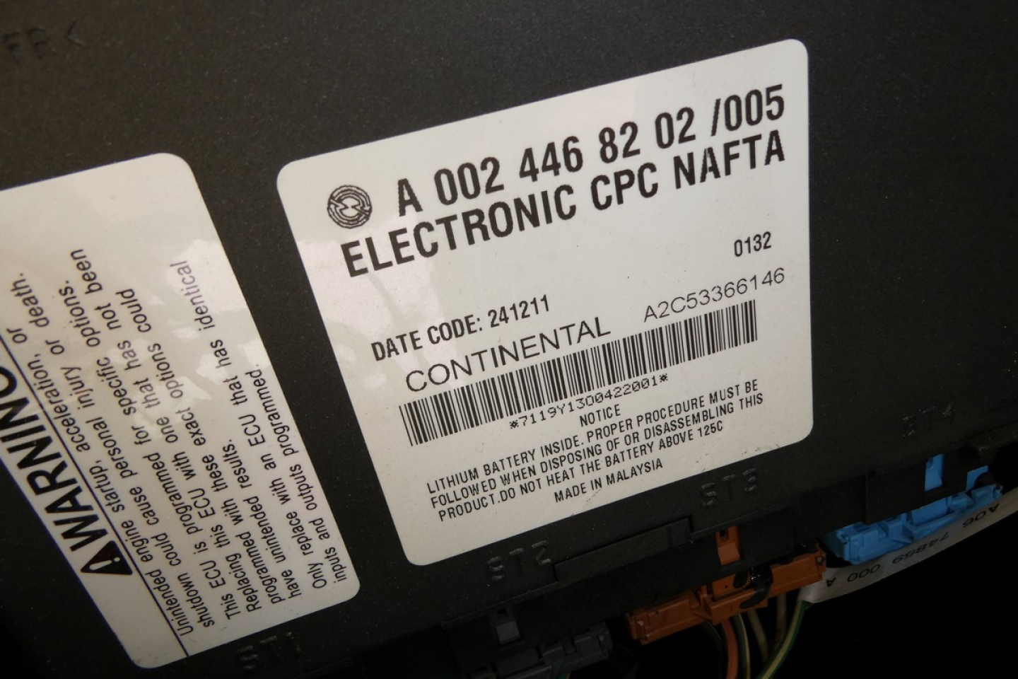 Label on a Freightliner truck component showing 'ELECTRONIC CPC NAFTA' and date code 241211, 'CONTINENTAL' and barcode text, plus warning labels and wires.