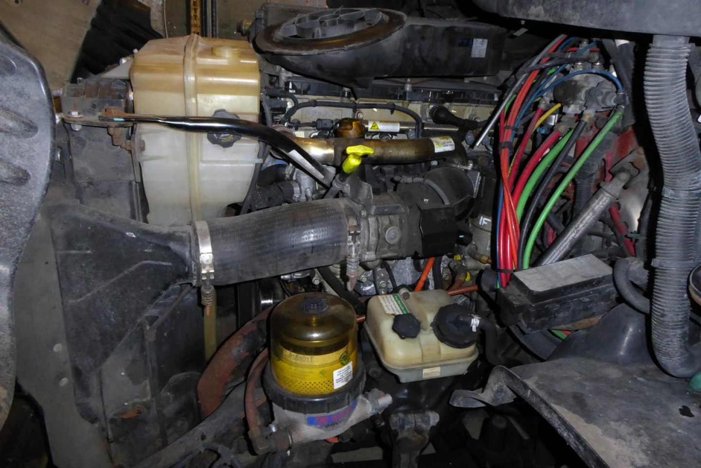 Diesel truck engine bay showing coolant reservoir, yellow-capped fluid containers, and wiring harness in Freightliner Cascadia cab