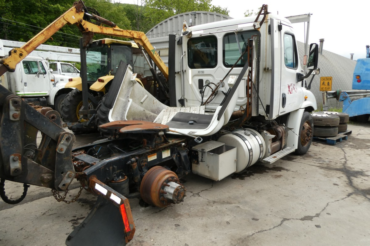 Truck cab and chassis of a Freightliner Cascadia 113 with exposed rear axle and removed wheels, side view with some equipment around.