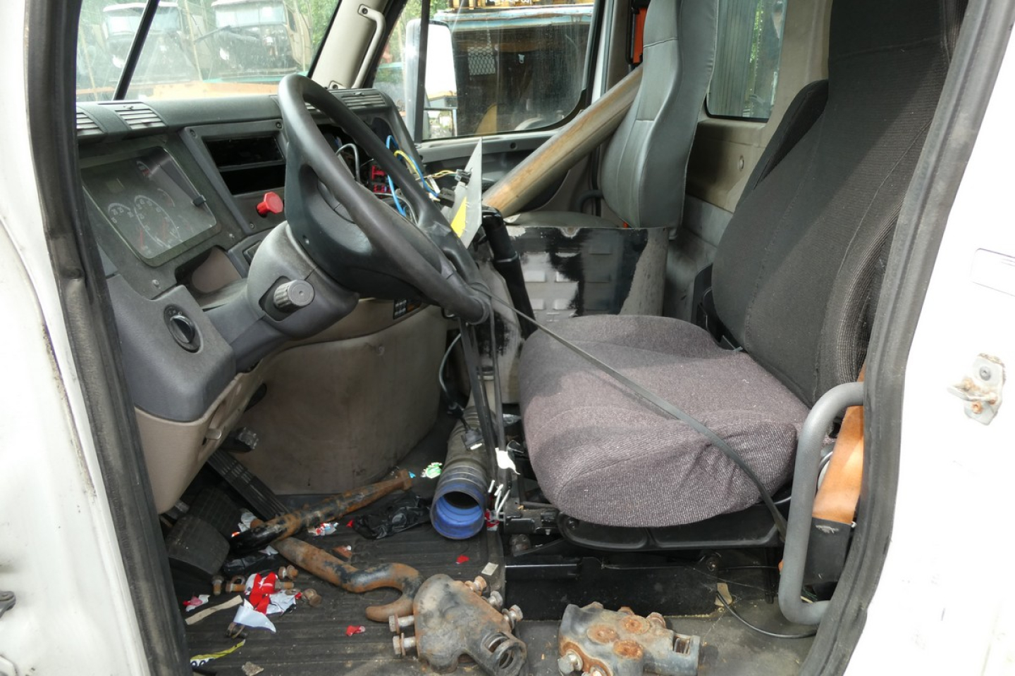 Cab interior of a 2012 Freightliner Cascadia 113 daycab showing steering wheel, driver seat, dashboard, and scattered floor debris.