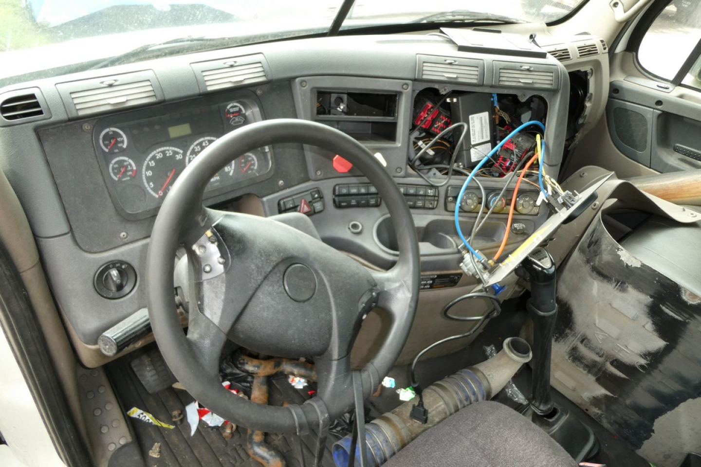 Dashboard and steering wheel inside Freightliner Cascadia cab showing exposed wiring and dashboard components.