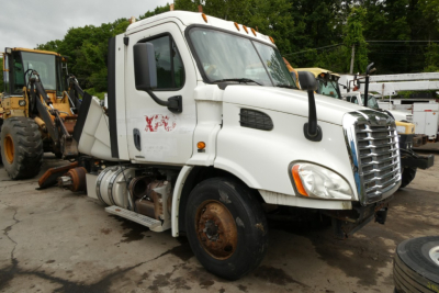 Truck cab showing front and side view of a white Freightliner Cascadia 113 Daycab with missing front wheel, engine bay, and drainage tanks.