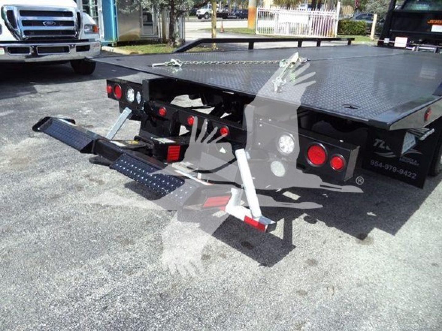 Truck rollback bed with rear-mounted steps and hydraulic system, platform and taillights visible.