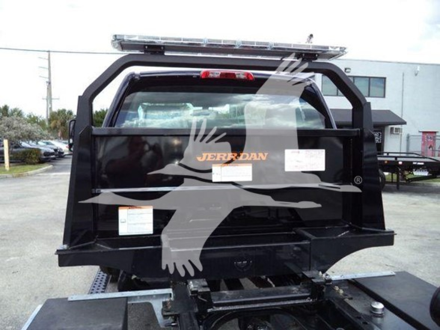 Trucks equipment showing a black rollback truck bed with frame, rear view, Jerr-Dan logo on side panel, white labels, and hitch area.